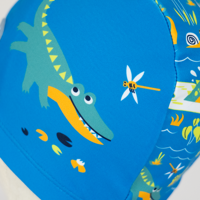 Baby swim hat in blue featuring crocodiles themed print.
