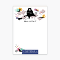 A colorful notepad with a cartoon image of a black cat and various playful illustrations such as a pencil, paper, and scissors. The text on the cover says 'DEAL WITH IT'.