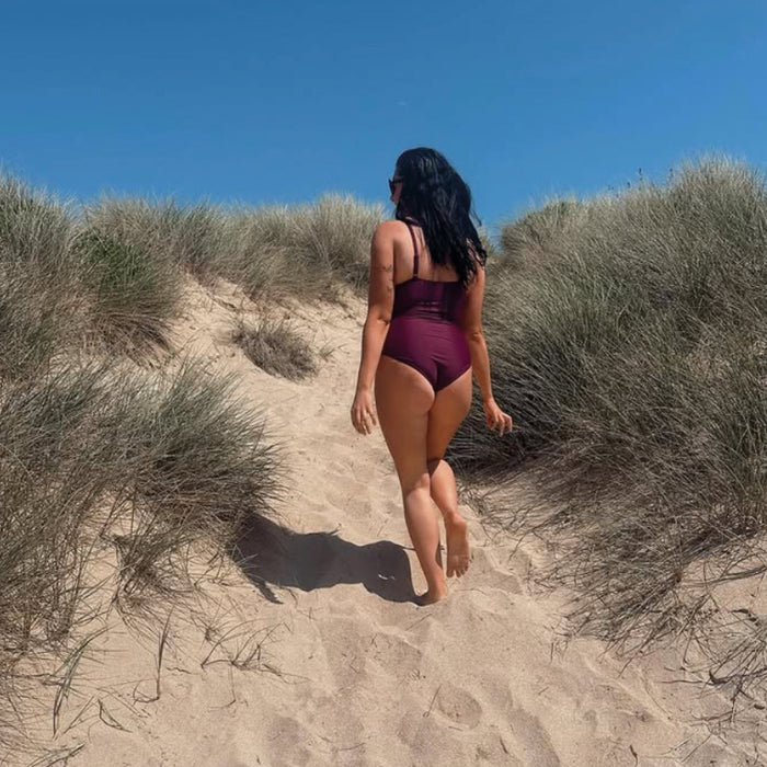Woman wearing plum swimming costume at the beach.
