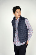 A man wearing a navy quilted button down vest with lapels, over a blue shirt, looking to the side.