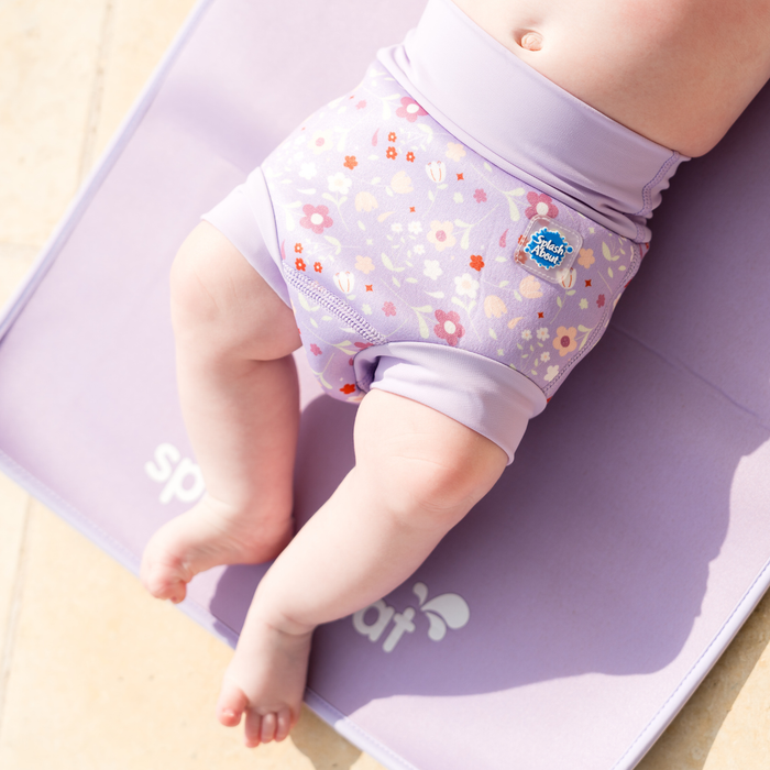 Child wearing reusable swim diaper in lilac and floral themed print. Front.