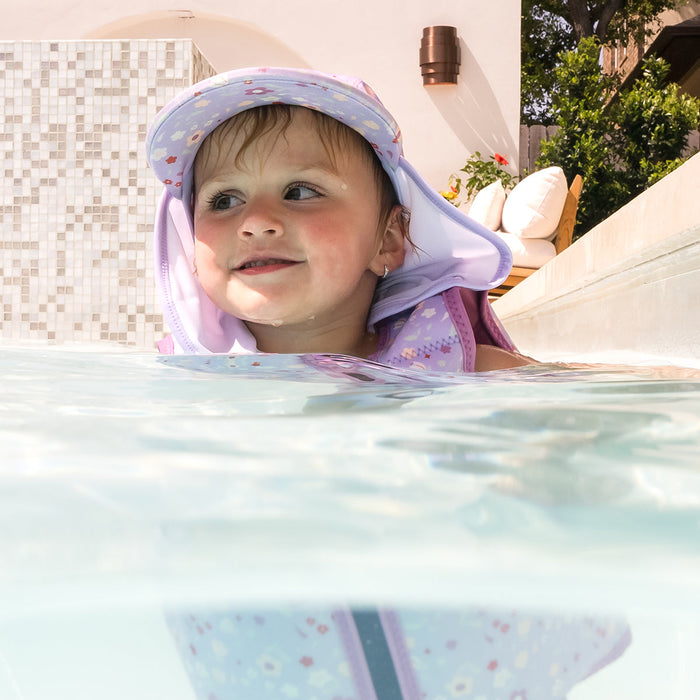 Little one wearing legionnaire style sun hat in lilac, with floral themed print panel. They are also wearing matching swim vest.