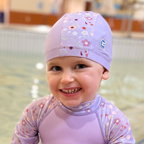 Little one wearing baby swim hat in lilac featuring floral themed print.