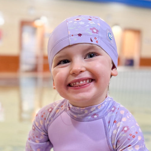 Little one wearing baby swim hat in lilac featuring floral themed print.
