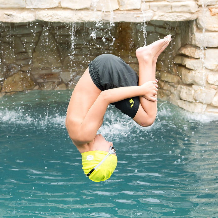 Kid jumping into the pool wearing yellow silicone swim cap.