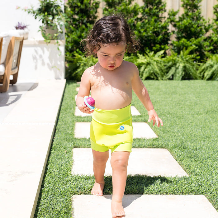 Little one wearing neoprene swim diaper in bright lime green, poolside.