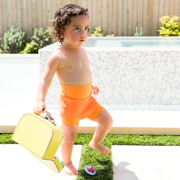 Little one wearing neoprene swim diaper in bright orange, poolside.