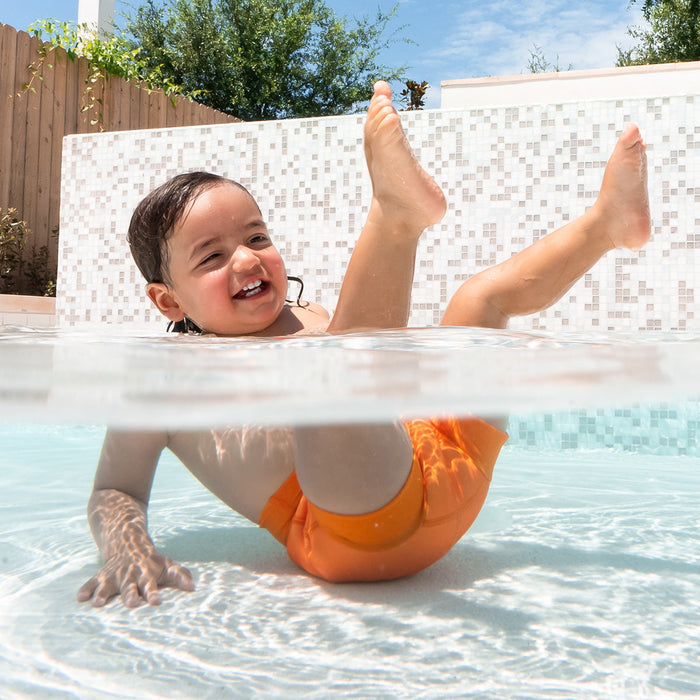 Little one swimming in neoprene swim diaper in bright orange.