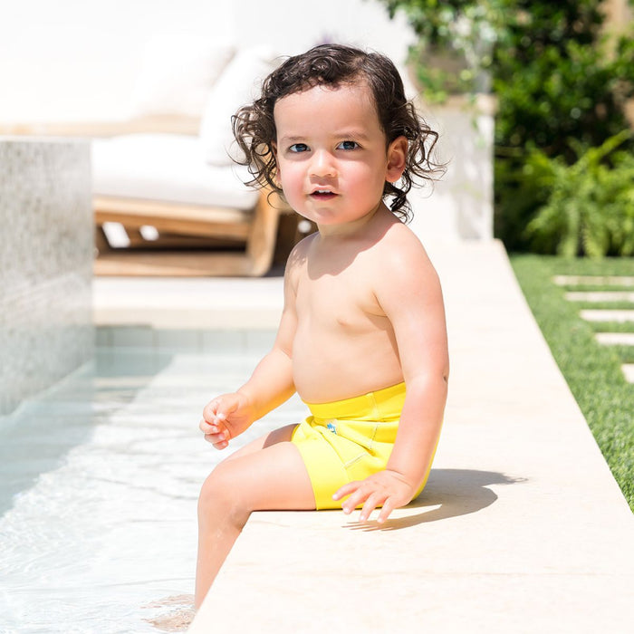 Little one wearing neoprene swim diaper in bright yellow, poolside.