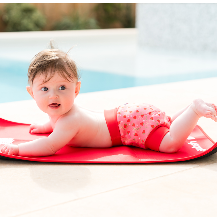 Baby wearing reusable swim diaper in pink with red ribs and strawberries themed print. Side