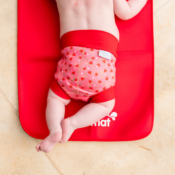 Baby wearing reusable swim diaper in pink with red ribs and strawberries themed print. Back