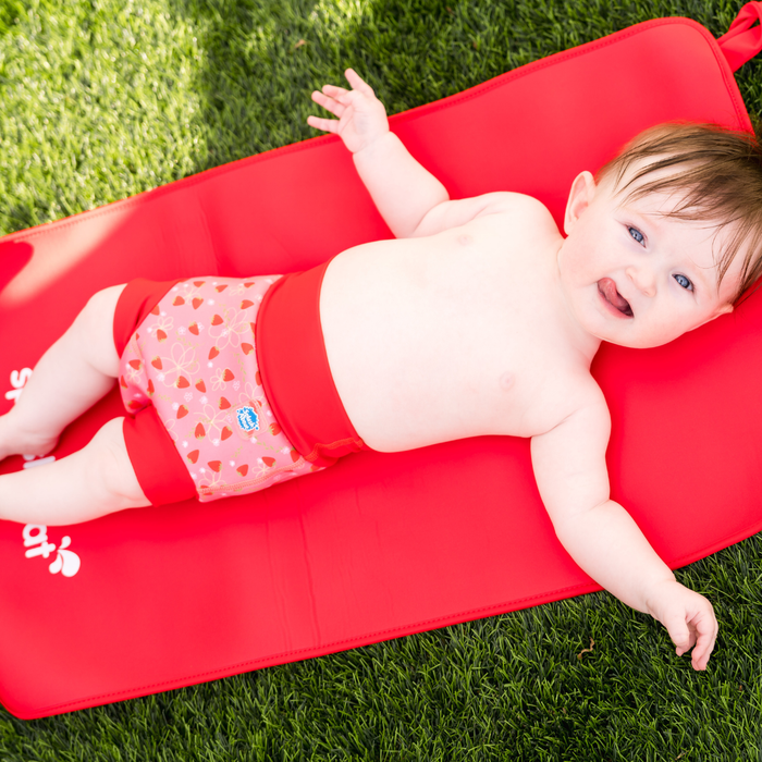 Baby wearing reusable swim diaper in pink with red ribs and strawberries themed print. Front