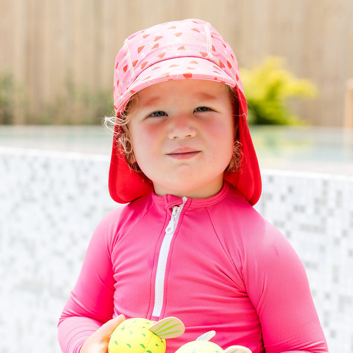 Little one wearing legionnaire style sun hat in pink and red, with strawberries themed print panel.