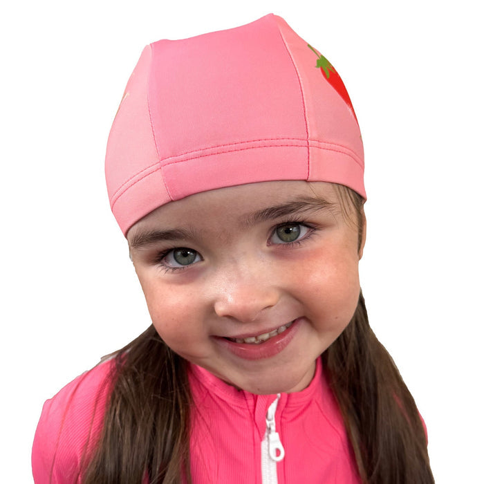 Little one wearing baby swim hat in pink featuring strawberries themed print.