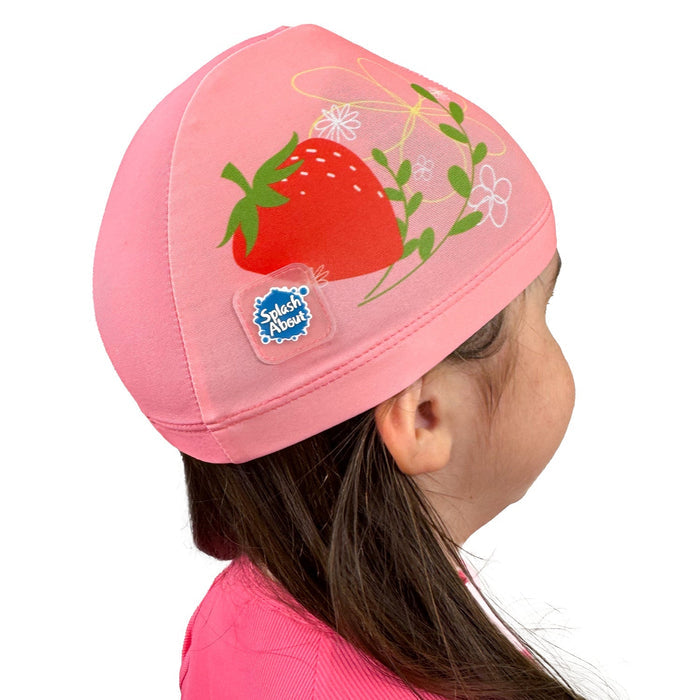 Little one wearing baby swim hat in pink featuring strawberries themed print.