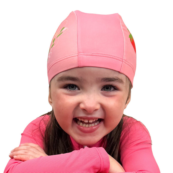 Little one wearing baby swim hat in pink featuring strawberries themed print.