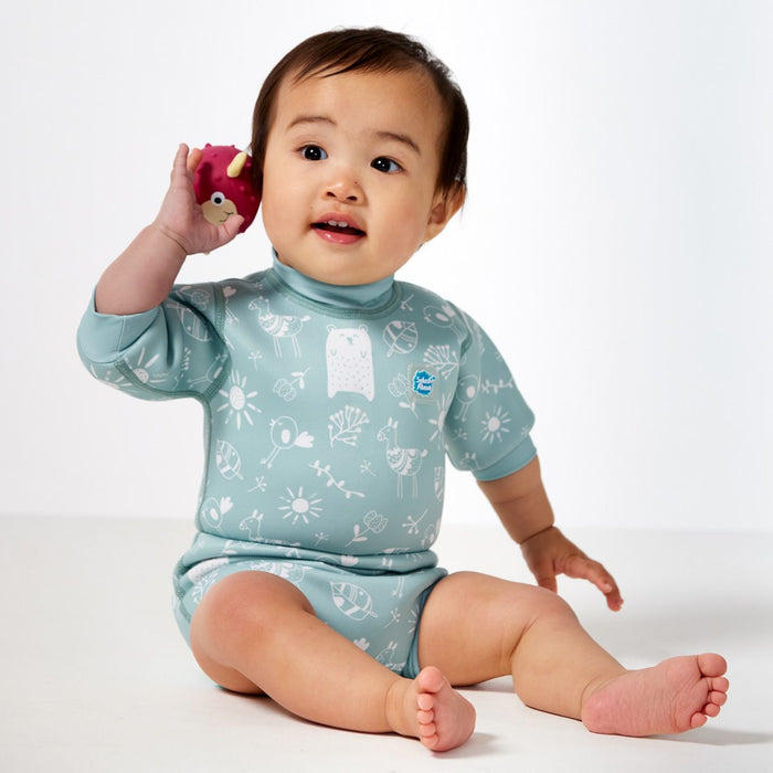 Lifestyle image of child wearing a baby wetsuit with built in swim diaper in greenish blue with animals themed print, including bears, birds and llamas. Front.