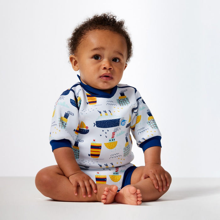 Lifestyle image of child wearing a baby wetsuit with built in swim diaper in white with navy trims and boats themed print. Front.