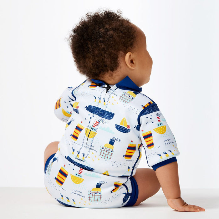 Lifestyle image of child wearing a baby wetsuit with built in swim diaper in white with navy trims and boats themed print. Back.