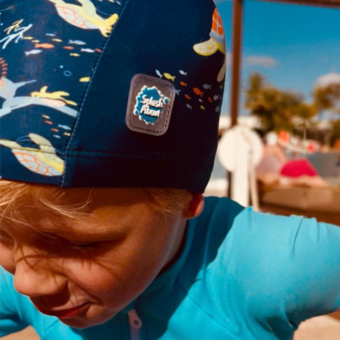 Child wearing baby swim hat in navy featuring turtles themed print.