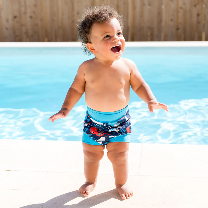 Child wearing reusable swim diaper in navy with cyan ribs and sea creatures themed print. Front.